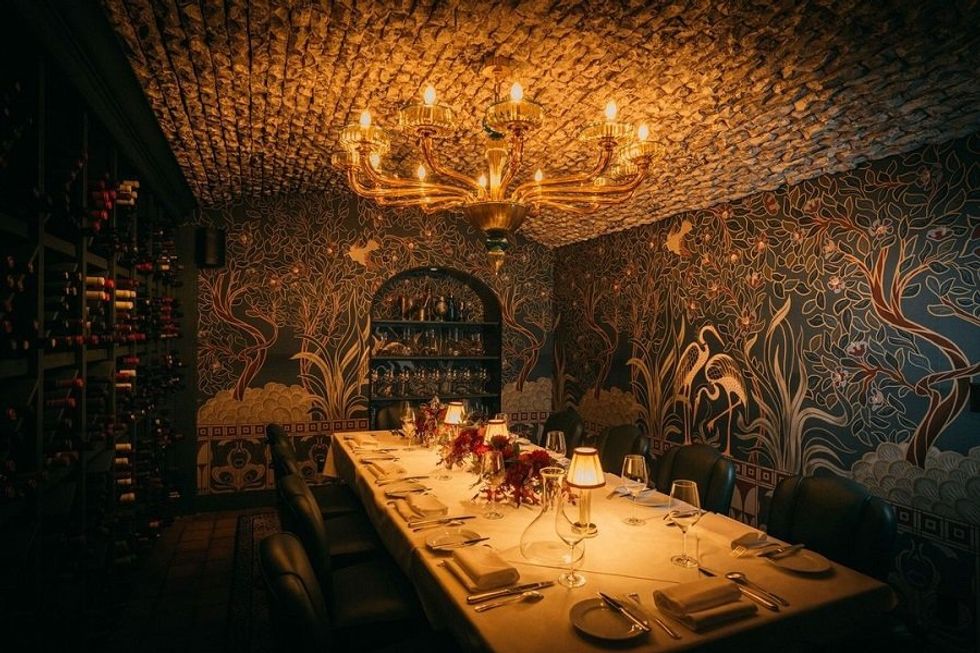 Elegant dining room with mural walls, chandeliers, and a wine rack.