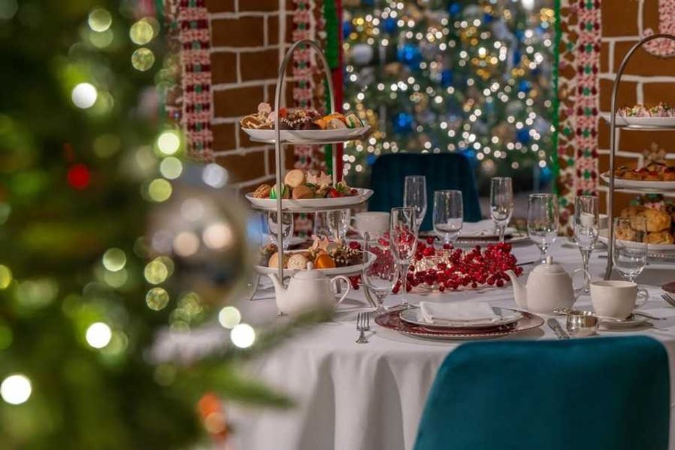Elegant holiday table setting with tiered trays, festive decor, and a blurred Christmas tree.