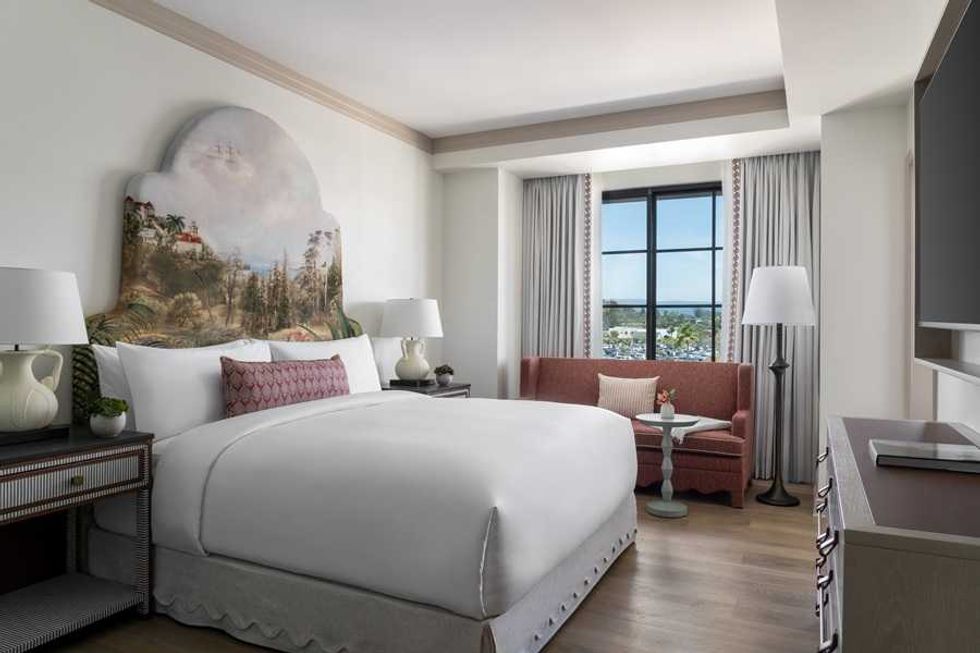 Elegant hotel room with a large bed, artwork headboard, sofa, and window view.