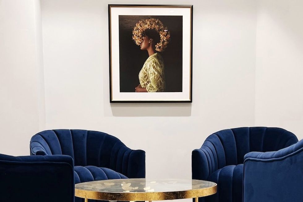 Elegant lounge with blue chairs, gold table, and portrait of a woman on the wall.