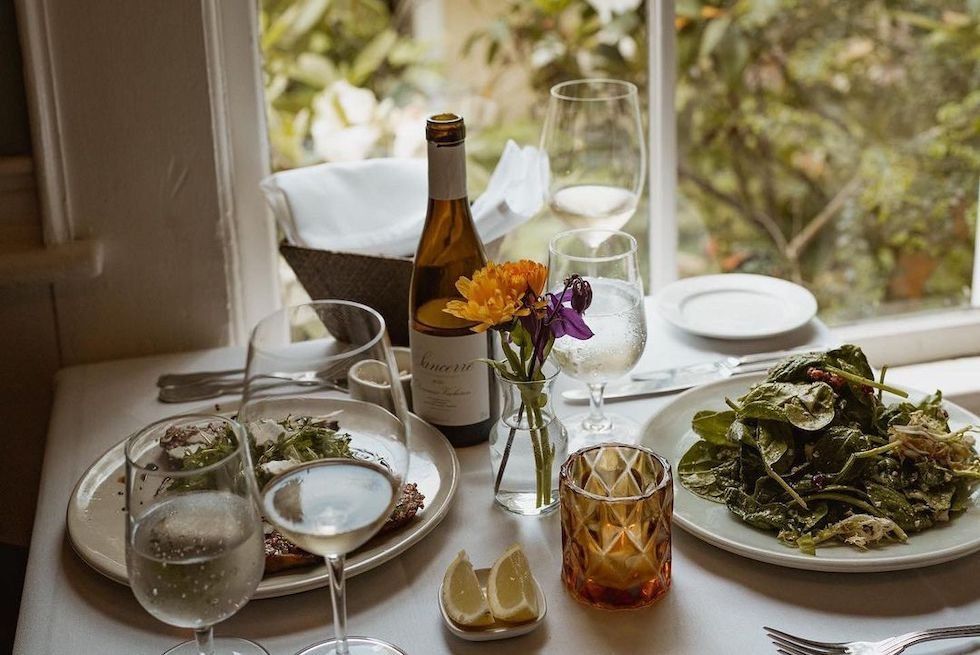 Elegant lunch by a window with wine, salad, and flowers on a white tablecloth.
