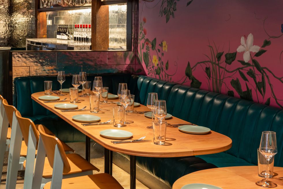 Elegant restaurant setting with a floral mural, teal seating, and table set for dining.