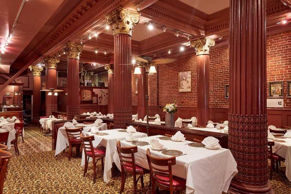Elegant restaurant with ornate columns, red brick walls, white tablecloths, and decorative chairs.
