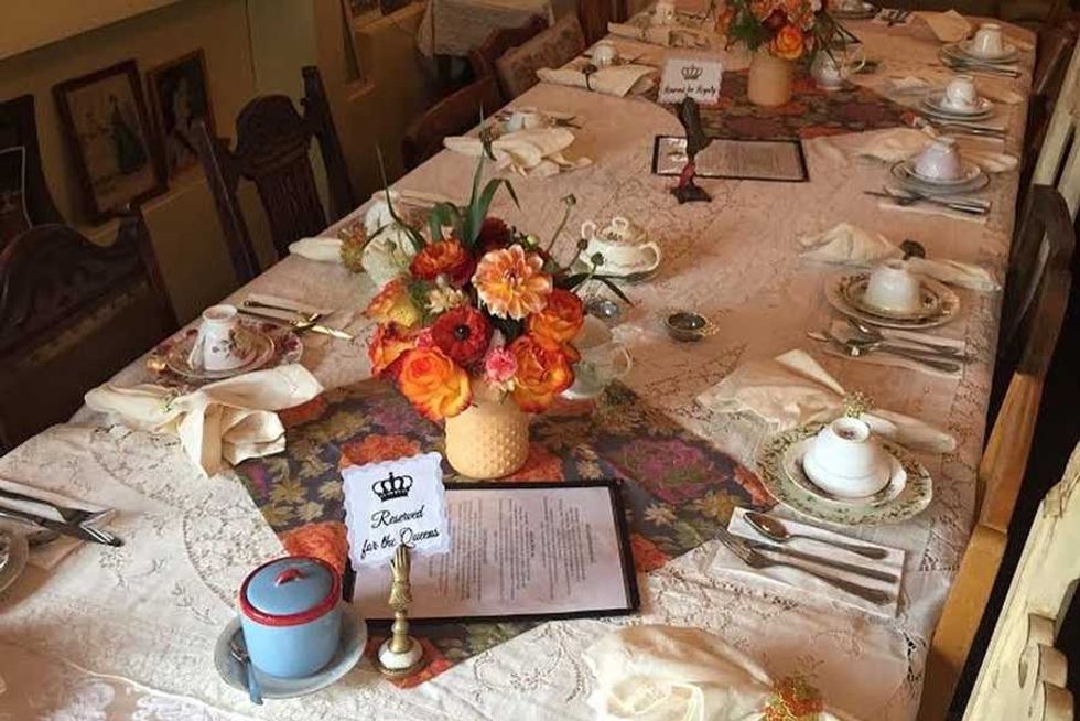 Elegant table set for tea with flowers, teacups, and "Reserved for the Queens" sign.