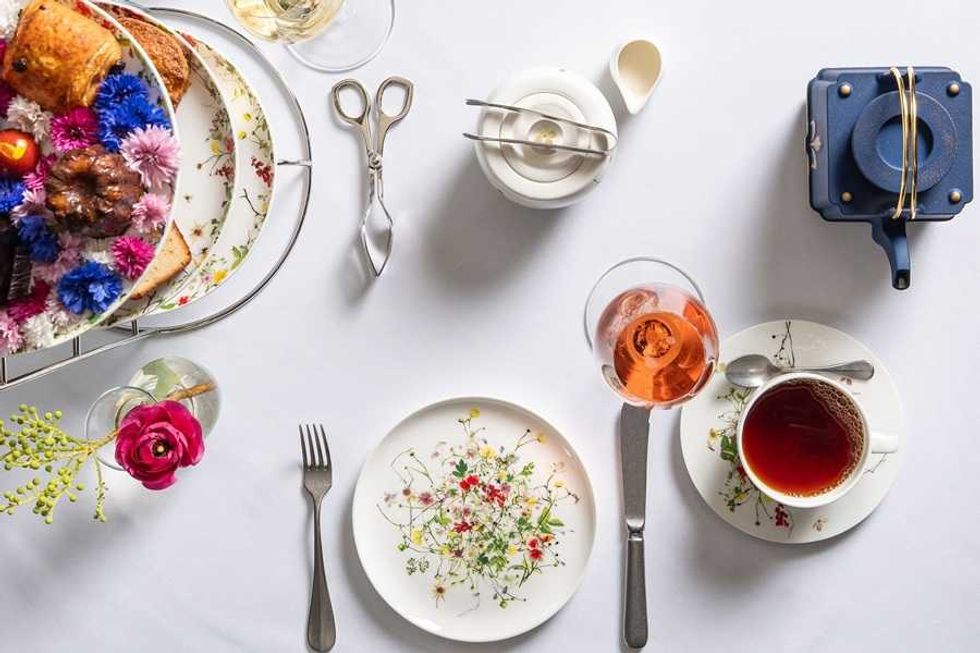 Elegant tea set with pastries, flowers, and tea on plates with floral designs.