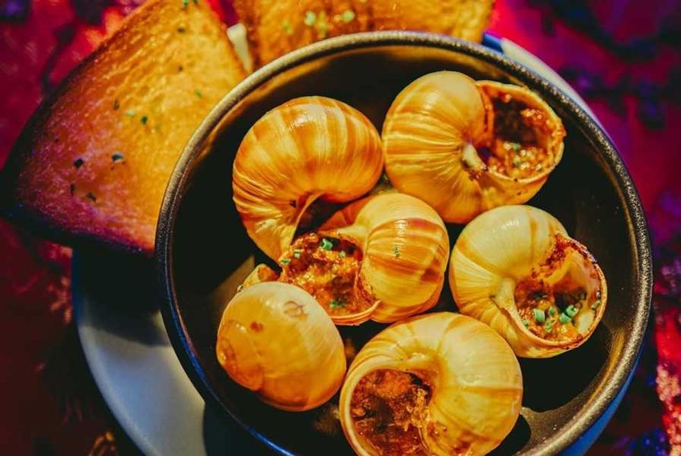 Escargot in shells with herbs, served with toasted bread in a bowl.