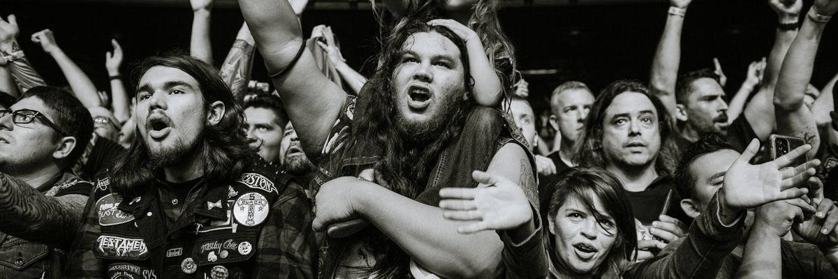 Excited concert crowd cheering and raising hands at a music event.