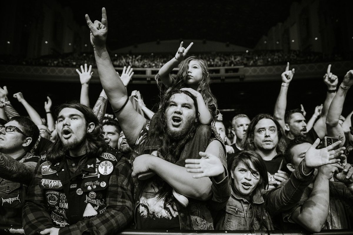 Excited concert crowd cheering and raising hands at a music event.