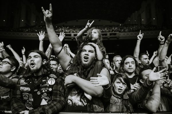 Excited concert crowd cheering and raising hands at a music event.