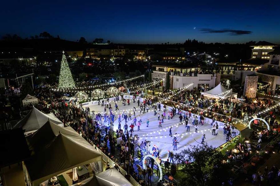 Festive ice skating rink at night with crowds and a large lit Christmas tree.