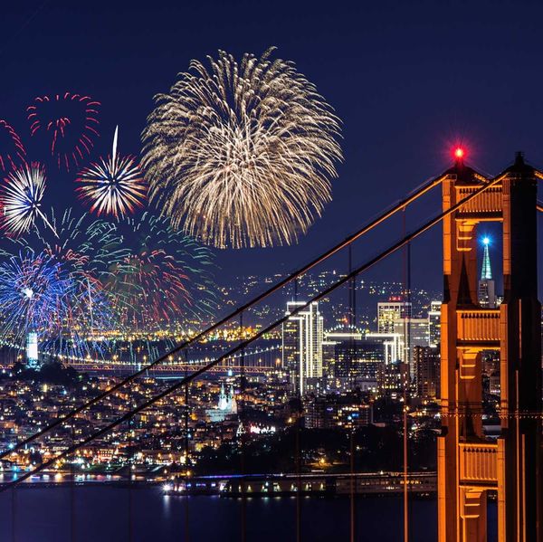 fireworks exploding over the lit up city of san francisco with golden gate bridge