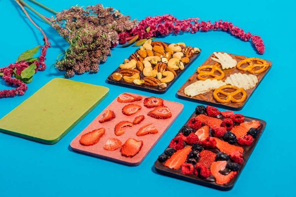 Five chocolate bars with nuts, berries, and pretzels on a blue background with flowers.