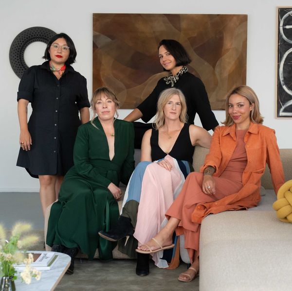 Five women pose in a stylish, modern living room with abstract art.