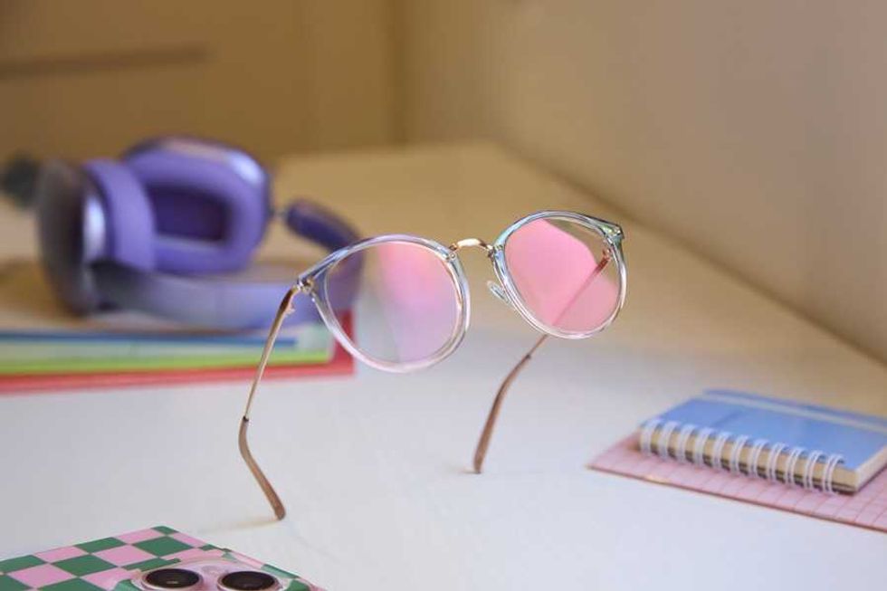 Floating glasses with pink lenses, notebooks, and purple headphones on a desk.