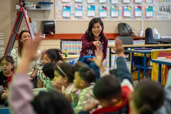 former ice skating champion Kristi Yamaguchi at the front of a kindergarten class pointing at a kid with a raised arm