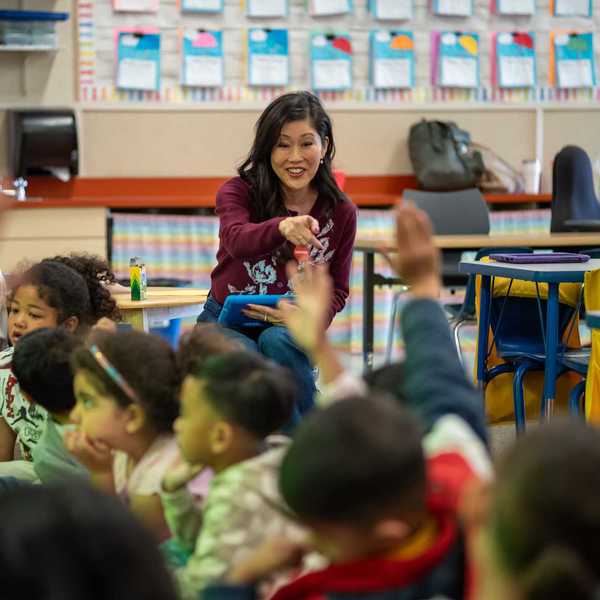 former ice skating champion Kristi Yamaguchi at the front of a kindergarten class pointing at a kid with a raised arm