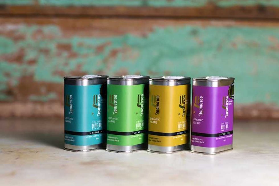 Four colorful tins of organic olive oil on a rustic wooden surface.