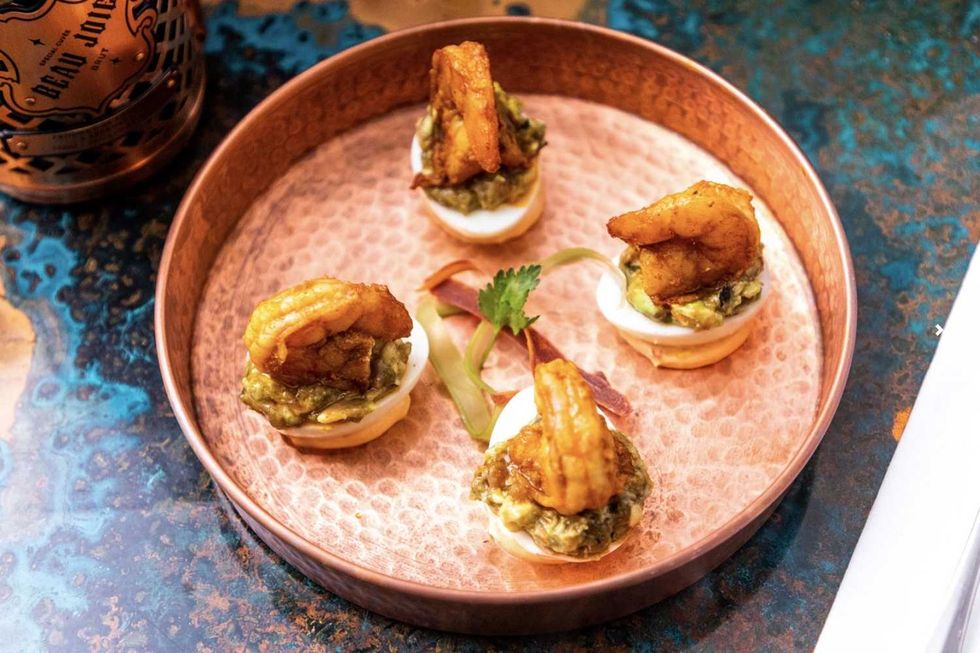 Four deviled eggs with shrimp and guacamole on a copper plate.