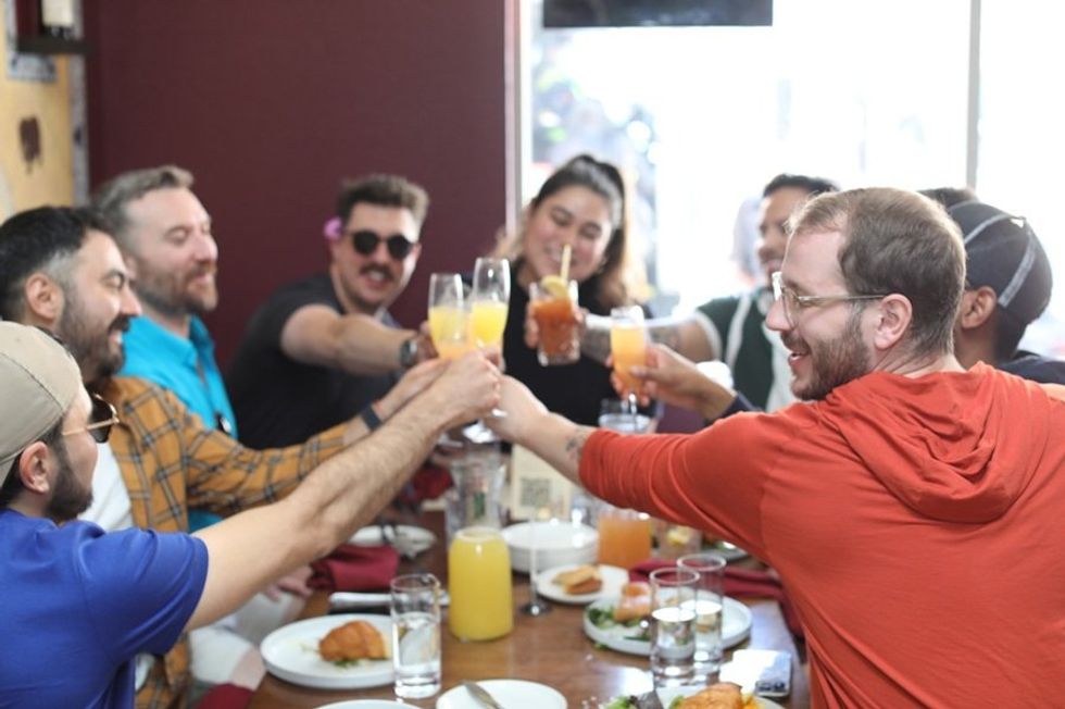 Friends toast with drinks around a table in a lively restaurant setting.