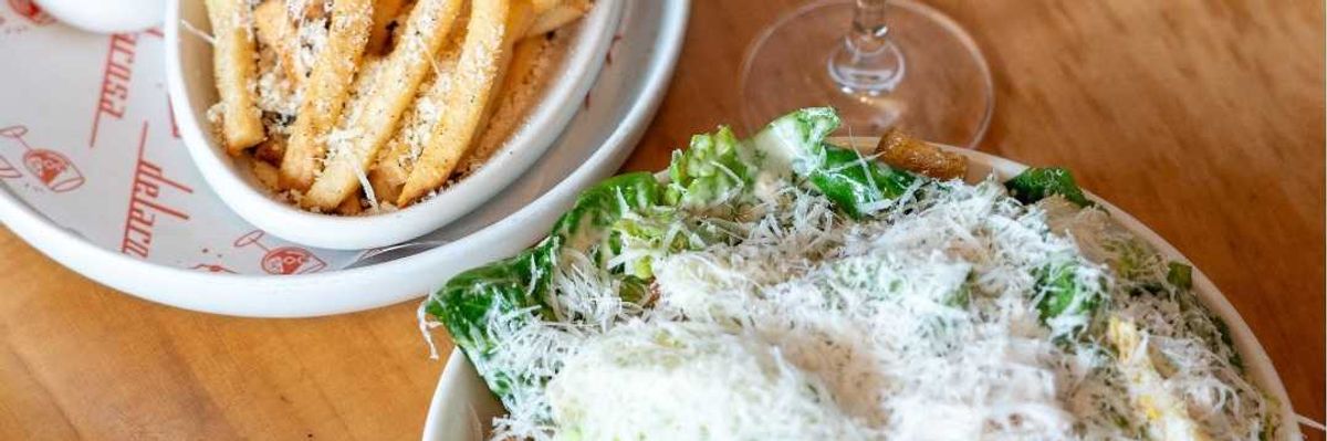Fries with sauce, Caesar salad, and a cocktail with olives on a wooden table.