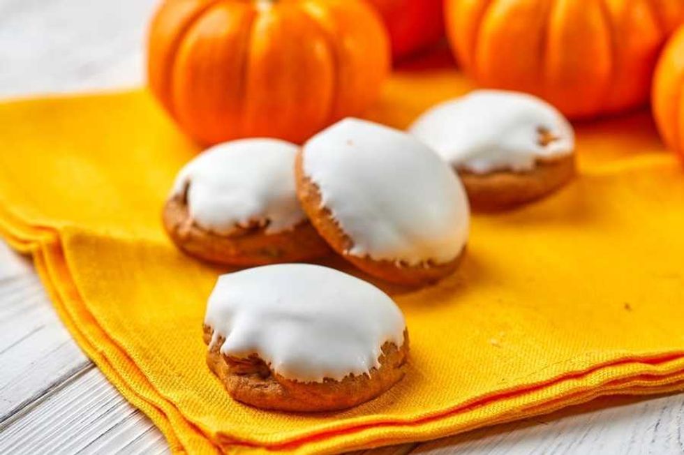 Frosted cookies on a yellow cloth, surrounded by small orange pumpkins.