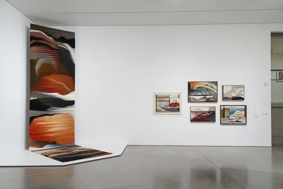 Gallery wall with abstract rugs and framed artwork in earthy tones.
