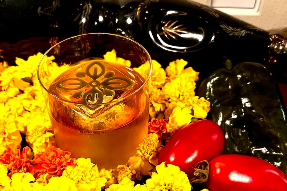 Glass with floral ice cube surrounded by marigolds and peppers.