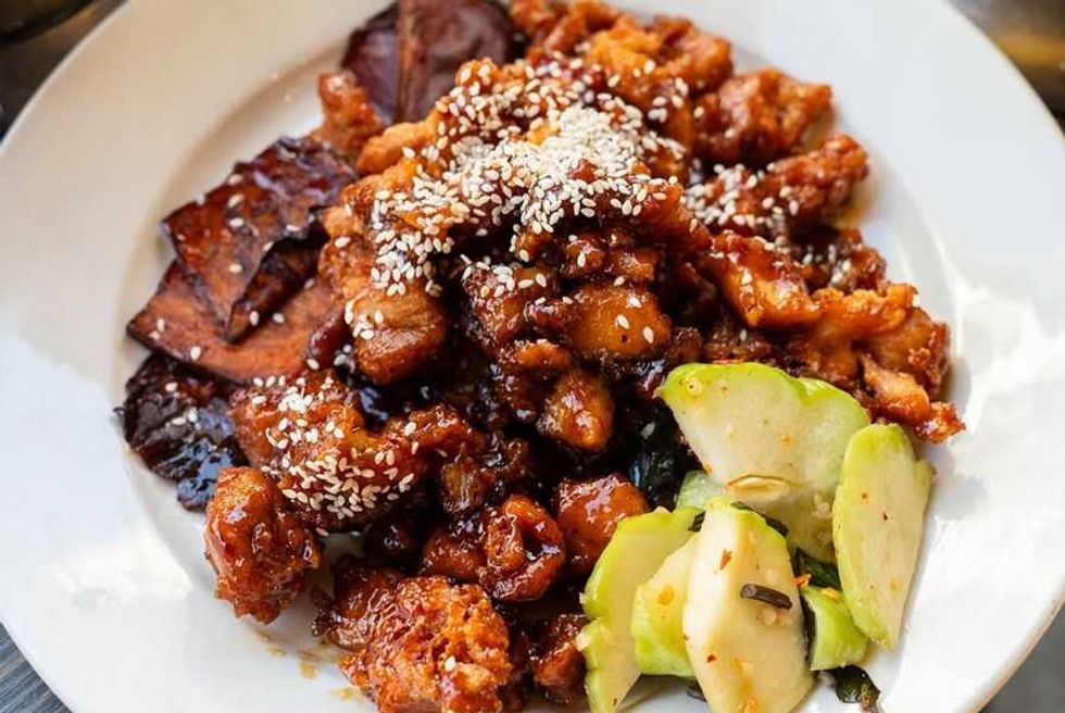 Glazed chicken with sesame seeds, dried eggplant, and pickles on a white plate.