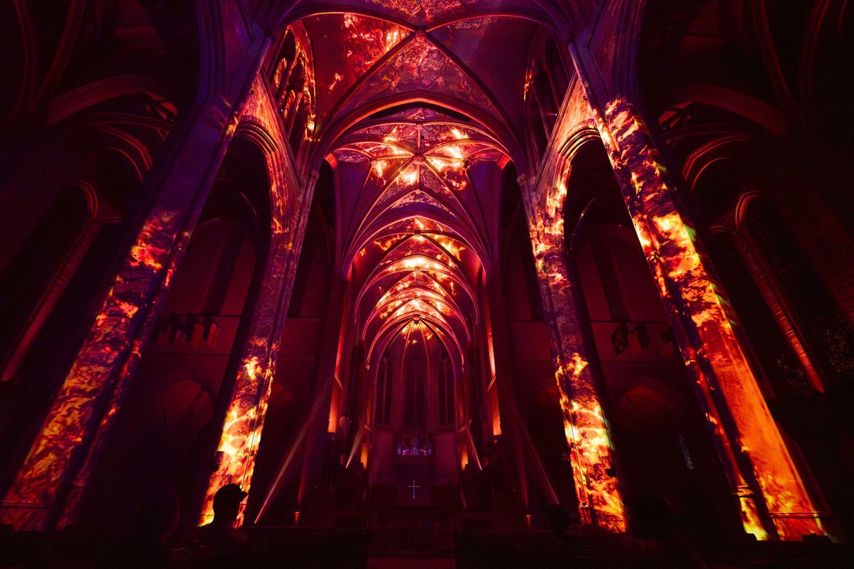 Gothic cathedral interior illuminated with fiery red and orange projections.