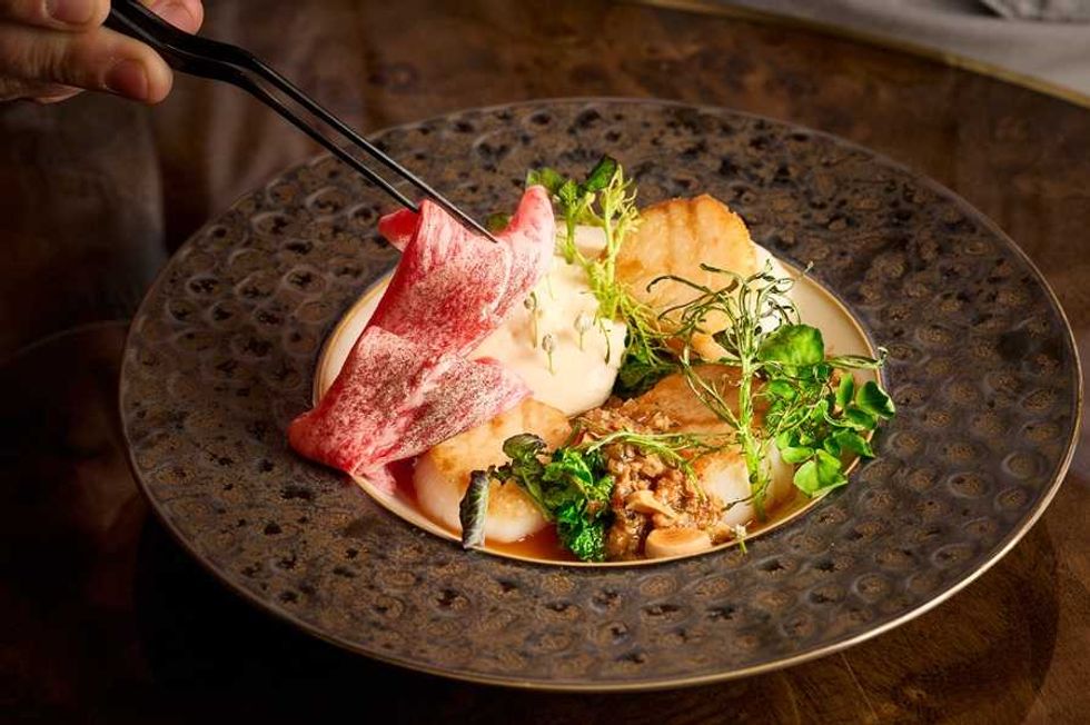 Gourmet dish with leafy greens, seared halibut, and wagyu beef on an elegant plate.