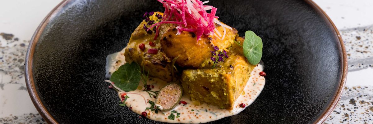 Gourmet dish with marinated cubes, sauces, pink garnish, and greens on a dark plate.