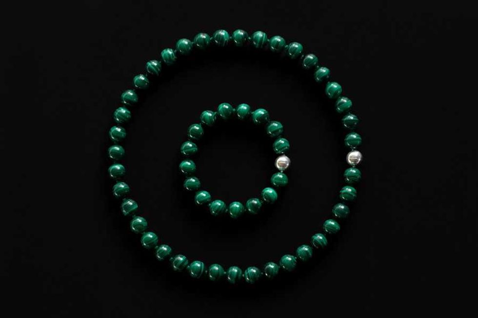 Green and silver beaded necklace and bracelet on a black background.