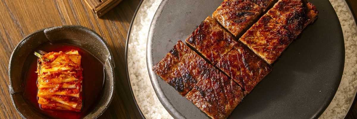 Grilled beef slices, kimchi, fried rice, and green garnish on a wooden table.