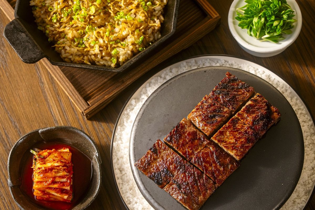 Grilled beef slices, kimchi, fried rice, and green garnish on a wooden table.