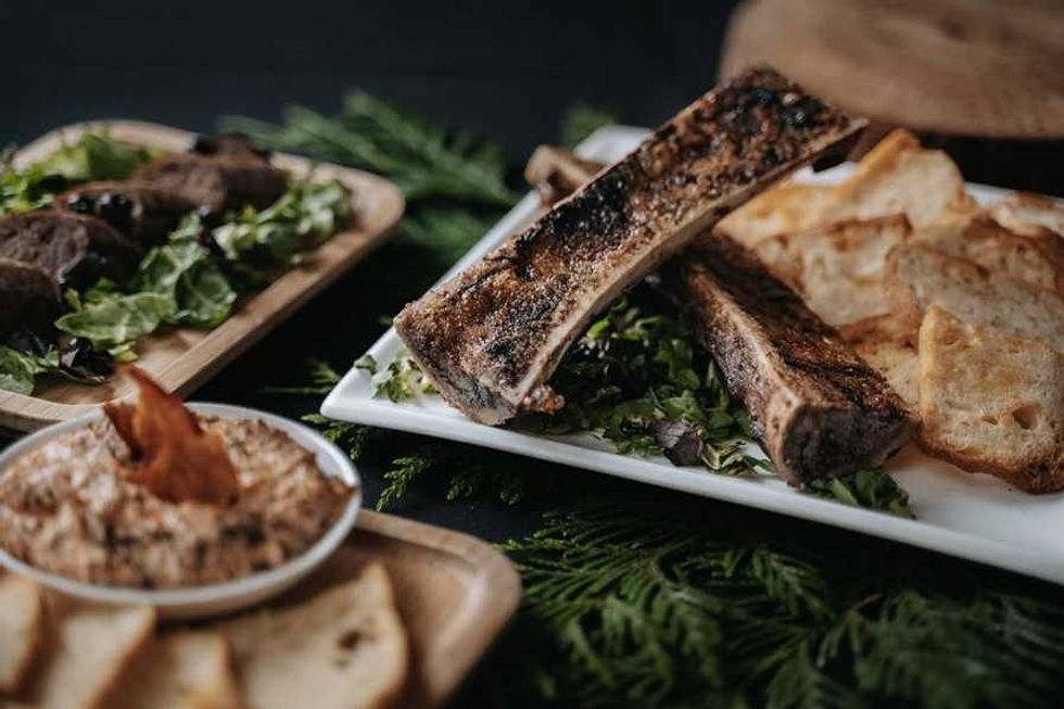 Grilled bone marrow with toast, salad, and dip on a table with leafy garnishes.
