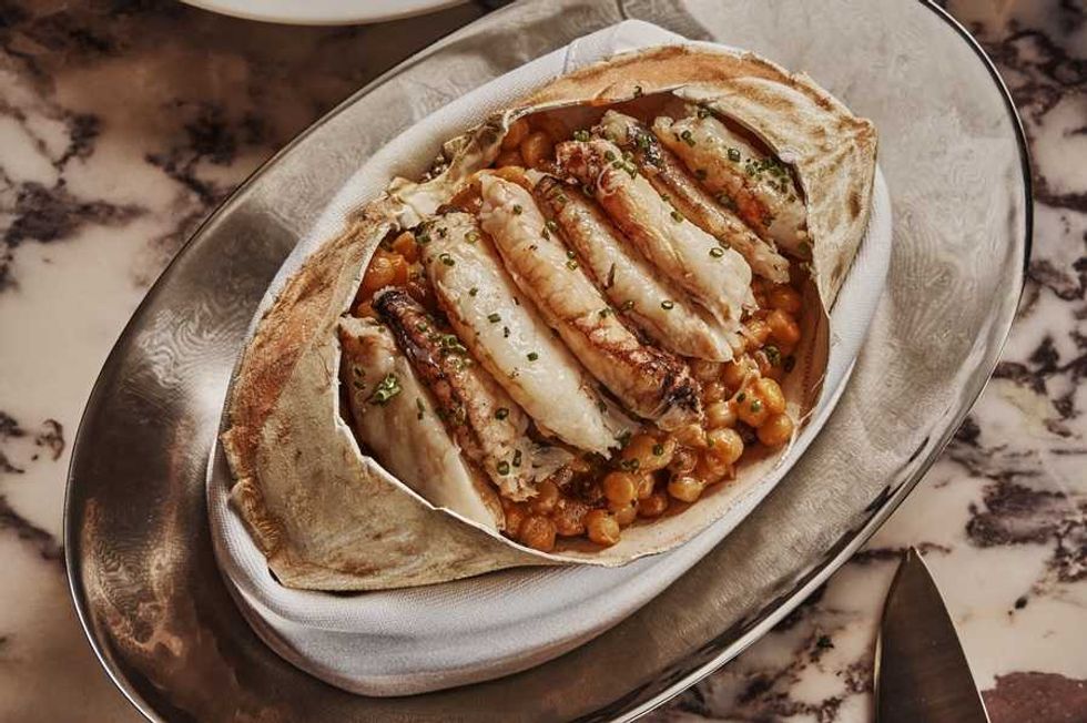 Grilled fish with chickpeas served in a crab shell on a marbled table setting.