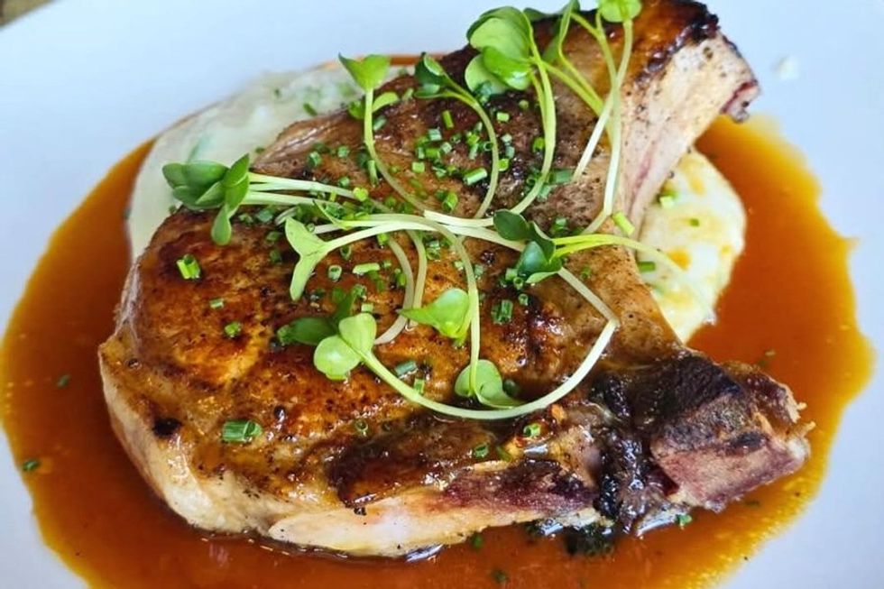 Grilled pork chop with microgreens over mashed potatoes and brown sauce on a white plate.
