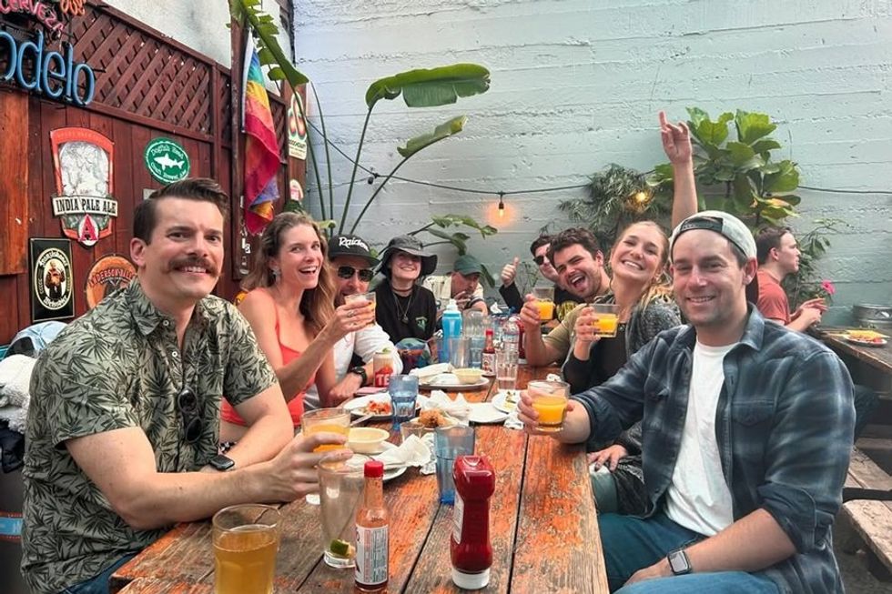 Group of friends raising drinks, smiling at an outdoor table with decorations.