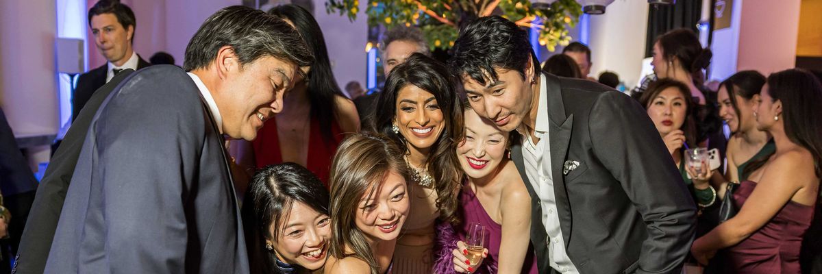 Group of people at a party taking a selfie together, smiling and dressed formally.