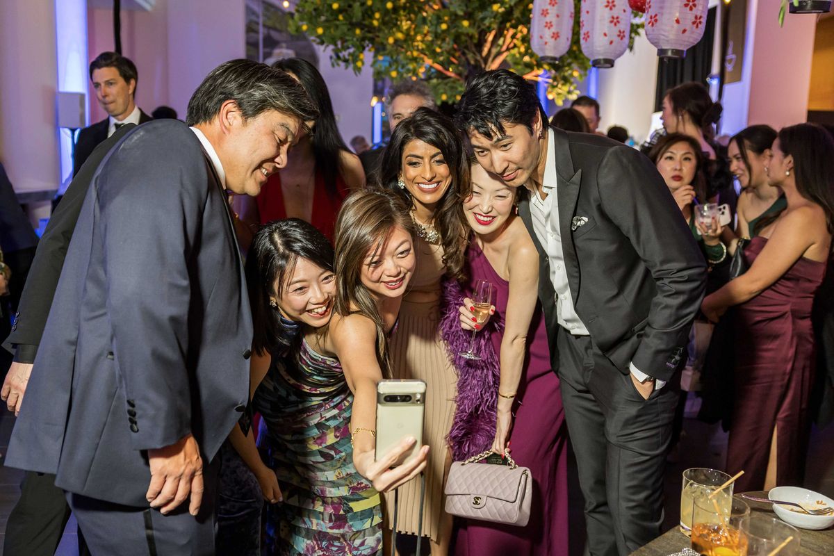 Group of people at a party taking a selfie together, smiling and dressed formally.