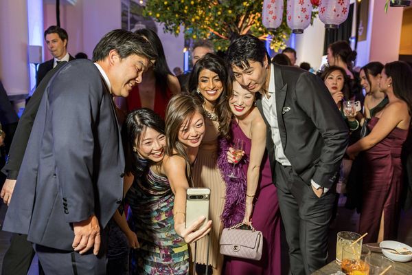 Group of people at a party taking a selfie together, smiling and dressed formally.