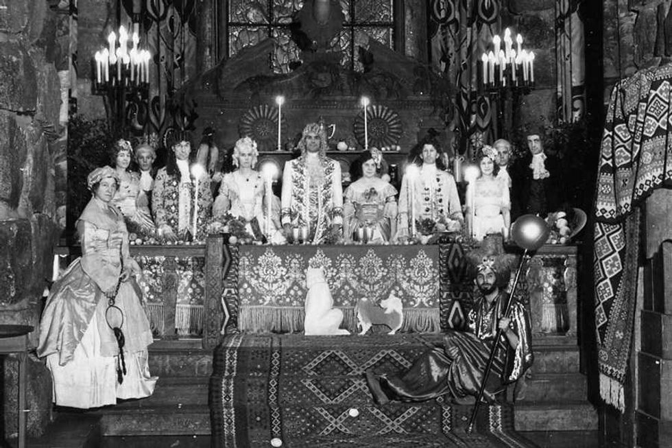 Group of people in ornate historical costumes at a lavishly decorated banquet table.
