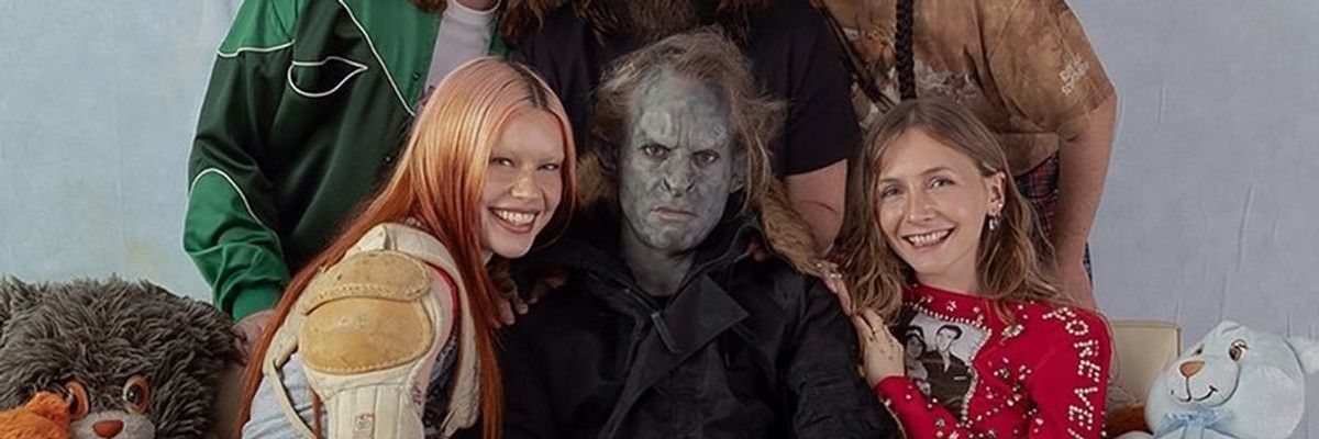 Group of people posing with stuffed animals, one person in costume, all smiling except one.