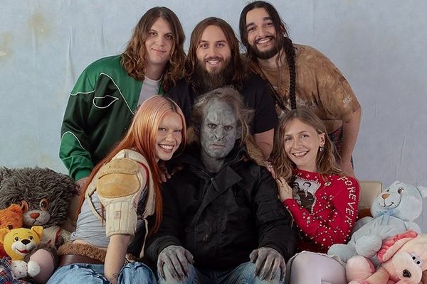 Group of people posing with stuffed animals, one person in costume, all smiling except one.