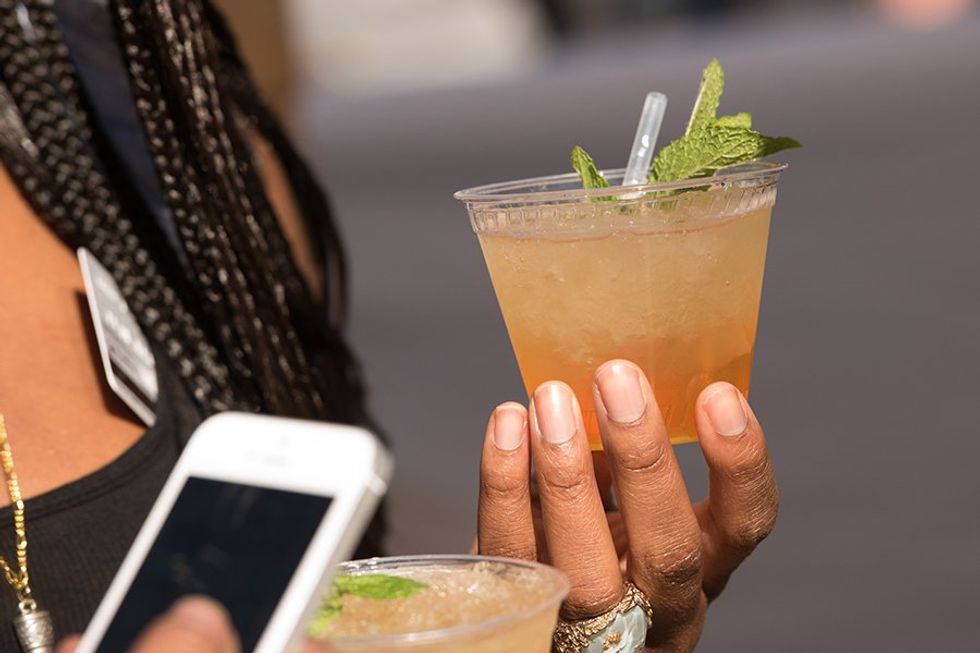 Hand holding a mint-garnished drink in a plastic cup, with a smartphone in the other hand.