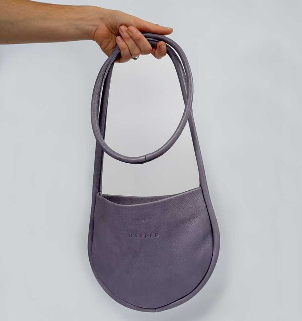Hand holding a purple crescent-shaped shoulder bag against a plain background.