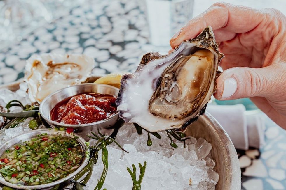 Hand holding an oyster, with sauces on ice.