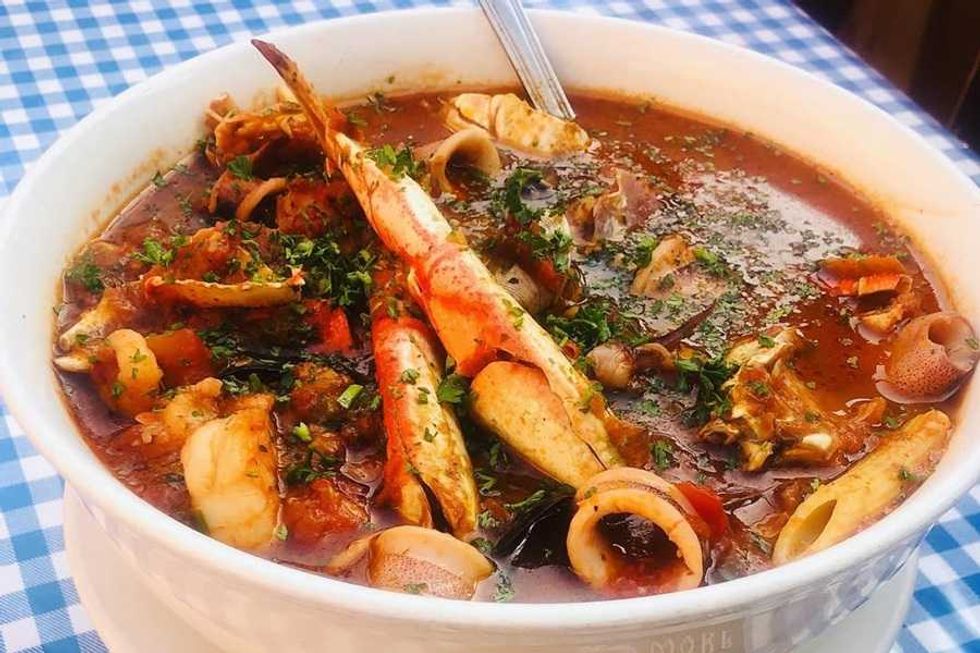 Hearty seafood stew in a bowl with crabs, herbs, and rich broth on a checkered tablecloth.