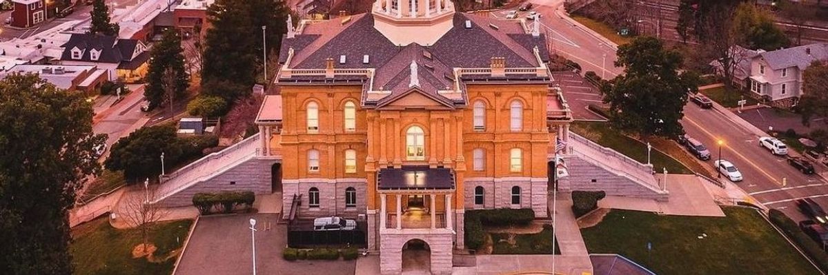 Historic courthouse under vibrant sunset sky, surrounded by roads and greenery.