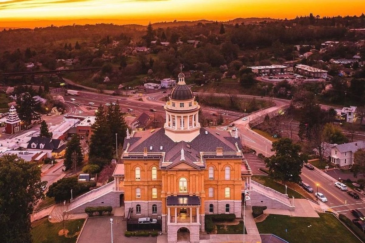 Historic courthouse under vibrant sunset sky, surrounded by roads and greenery.